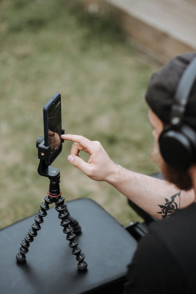 From above of crop anonymous male using mobile phone on tripod in yard in selective focus